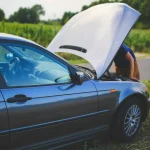 Osoba u porouchaného vozidla na dálnici s výstražným trojúhelníkem a vestou. Návod, co dělat při poruše auta na dálnici.