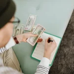 Ruce s kalkulačkou a mincemi na stole, symbolizující rozpočtování a tipy jak efektivně šetřit peníze v domácnosti.