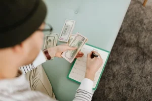 Ruce s kalkulačkou a mincemi na stole, symbolizující rozpočtování a tipy jak efektivně šetřit peníze v domácnosti.