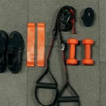 Šťastný pár drží různé sportovní vybavení, které představuje, jak vybrat správné sportovní vybavení pro začátečníky. Žena ukazuje na boty, muž drží raketu.