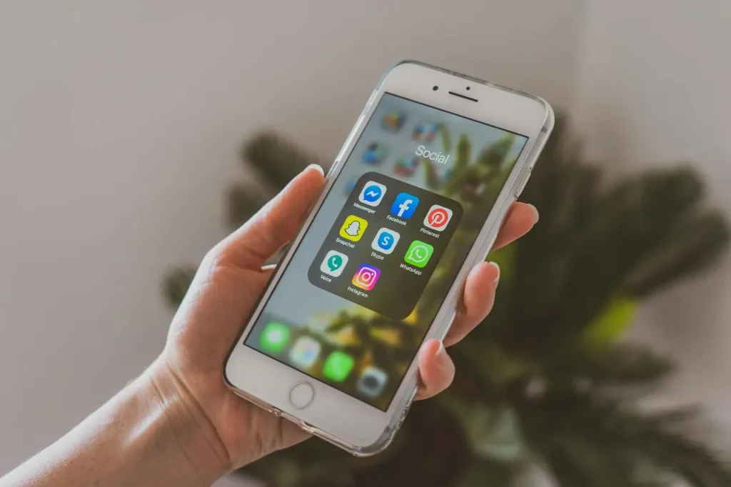 Mladá žena s vážným výrazem drží smartphone s ikonami sociálních médií, což symbolizuje potřebu ochrany osobních údajů na sociálních sítích.