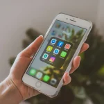 Mladá žena s vážným výrazem drží smartphone s ikonami sociálních médií, což symbolizuje potřebu ochrany osobních údajů na sociálních sítích.