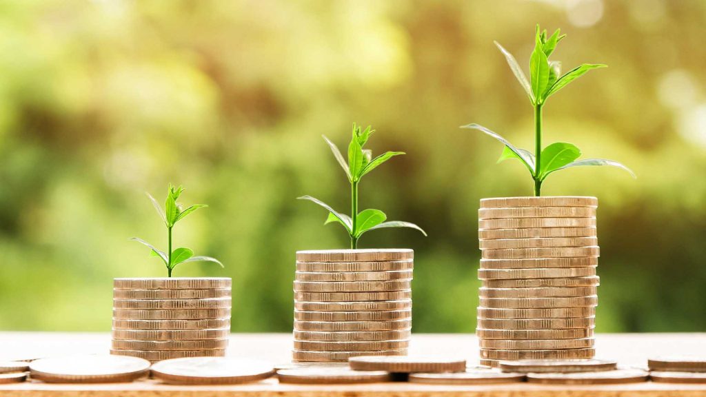 Drei wachsende Münzstapel mit sprießenden grünen Pflanzen symbolisieren das Wachstum von Ersparnissen oder Investitionen.