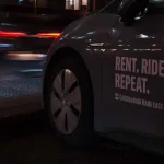 Joven desbloqueando un vehículo de carsharing con su smartphone en una calle urbana española, destacando la accesibilidad del renting y carsharing.