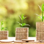 Trois piles croissantes de pièces de monnaie avec des plantes vertes qui poussent, symbolisant la croissance de l'épargne ou des investissements.