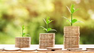 Trois piles croissantes de pièces de monnaie avec des plantes vertes qui poussent, symbolisant la croissance de l'épargne ou des investissements.