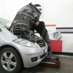 Férfi szerelő gondosan átvizsgál egy személygépkocsi motorterét, kiemelve a rendszeres autó karbantartás fontosságát a hosszú élettartamért.