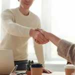Különböző nemzetiségű üzletemberek tárgyalnak modern irodában, ahol nemzetközi üzleti tárgyalástechnikai stratégiákról egyeztetnek, kivetített adatokat nézve.