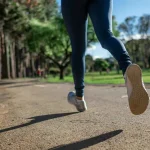 O alergătoare zâmbește în timp ce aleargă pe o alee verde, exemplificând bucuria mișcării, ideal pentru sfaturi începători alergat.