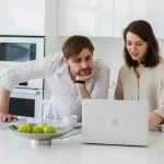 En person sitter vid ett bord med en laptop och papper, symboliserande processen för bostadssökning och granskning av hyresavtal.
