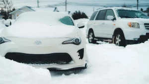 Auto sa opatrne pohybuje po zasneženej ceste s rozsvietenými svetlami, čo znázorňuje dôležité tipy na bezpečnú jazdu v zime.