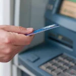 Osoba wkładająca kartę płatniczą do bankomatu.
